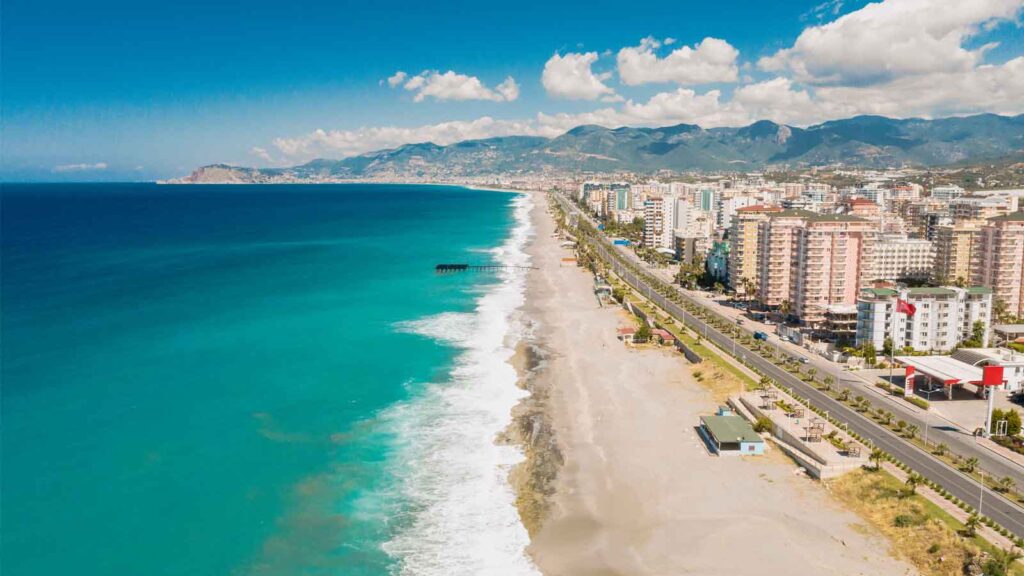 Konyaaltı Beach pebble shoreline with clear turquoise water, beachgoers, and snow-capped Taurus Mountains in background