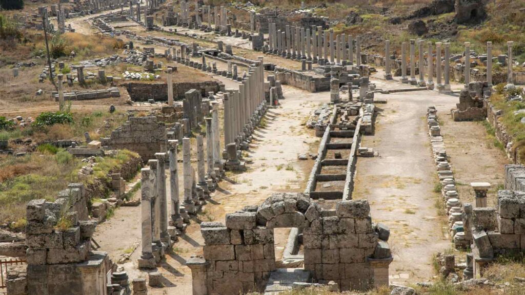 Perge archaeological site showing colonnaded Roman street with marble columns, ancient stadium, and Hellenistic gates