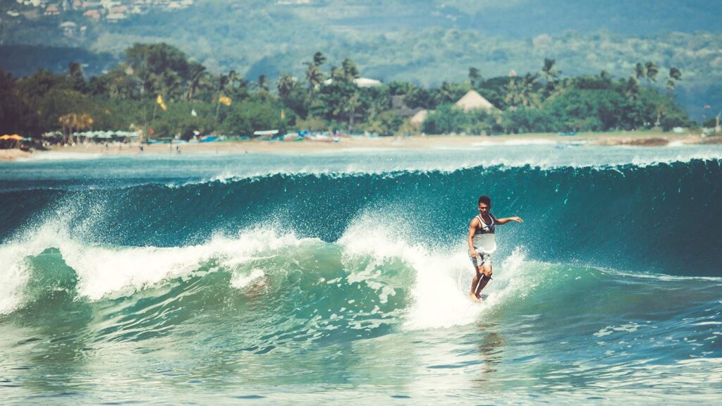  Surfers riding waves at Canggu beach with black volcanic sand and palm trees in background