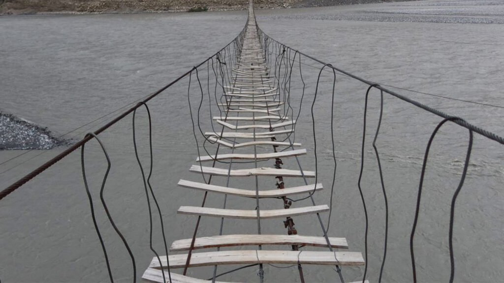 Tourists crossing the famous Passu Suspension Bridge over Hunza River with mountain peaks in background